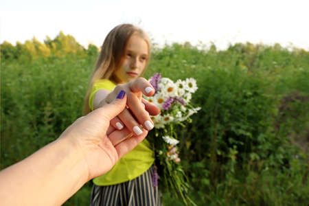 Mom's hand holds daughter's hand with a bouquet of daisies in summer in nature.の写真素材