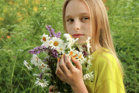 A blonde girl holding a bouquet of daisies in her hands on the background of nature.の写真素材