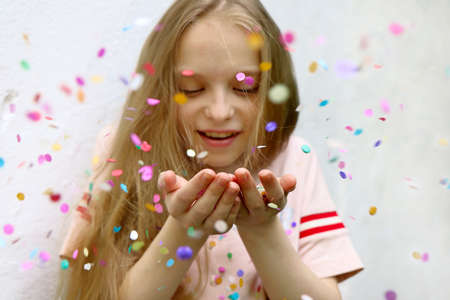 The blonde girl happily blows on the confetti in her hands in the summer.