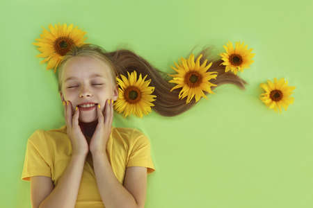 A beautiful girl with sunflowers in her blonde hair and a yellow baby manicure on a light green background.の写真素材