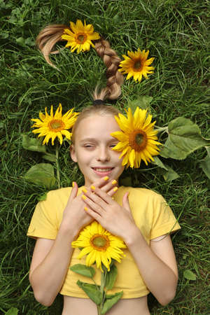 A beautiful girl with a yellow manicure lies on the grass with sunflowers.の写真素材