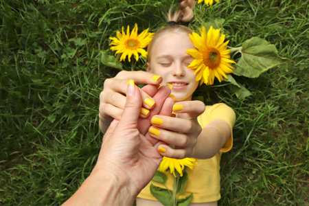 A beautiful girl with a yellow manicure lies on the grass with sunflowers.の写真素材