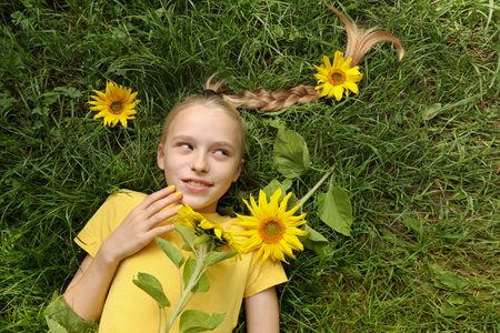 A beautiful girl with a yellow manicure lies on the grass with sunflowers.の写真素材