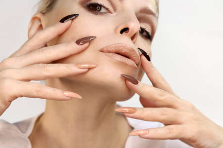 Brown and beige make-up and manicure on the long shape of the nails of a woman.の写真素材