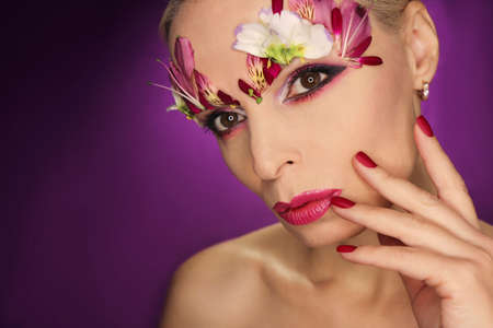 Burgundy red manicure and eye makeup with flower petals.の写真素材