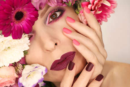 Burgundy pink manicure and makeup on a woman with a variety of flowers.