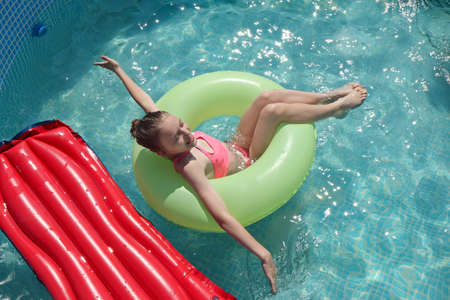 The girl happily swims in the pool with water in summer.の写真素材