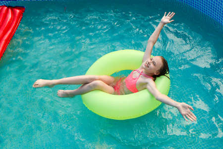The girl happily swims in the pool with water in summer.の写真素材