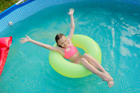 The girl happily swims in the pool with water in summer.の写真素材