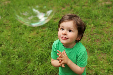 A little boy plays with soap bubbles in the summer outdoors.の写真素材