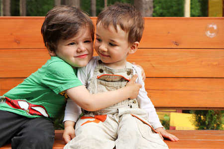 Two brothers sit in nature in the summer on a bench.の写真素材