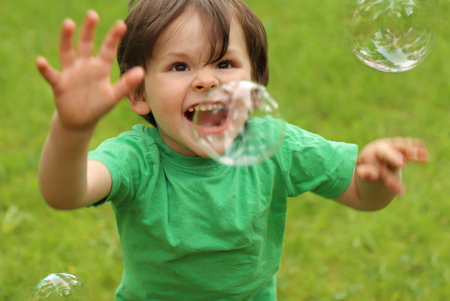 A little boy plays with soap bubbles in the summer outdoors.の写真素材