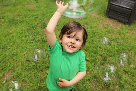 A little boy plays with soap bubbles in the summer outdoors.の写真素材