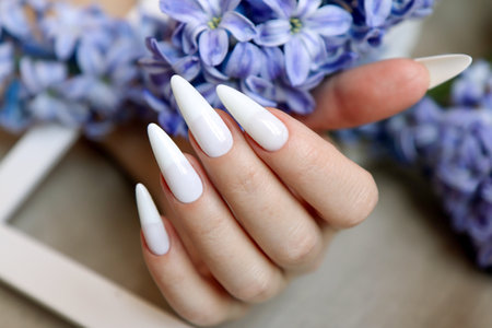 Female hand with white manicure and blue hyacinth flower.の写真素材