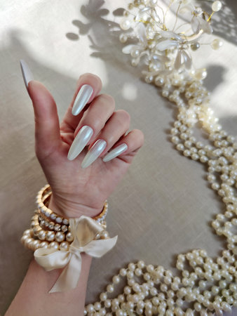 Female hand with long nails and white manicure with pearls and beadsの写真素材