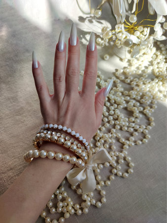 Beautiful female hand with white manicure and pearls on the tableの写真素材