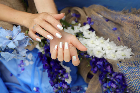 Pearl manicure on short square nails on a blue background with a bouquet of irises.の写真素材