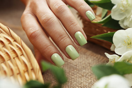 Women's hands with a green pastel manicure with jasmine on a wooden background with burlap.の写真素材