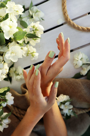 Women's hands with a green pastel manicure with jasmine on a wooden background with burlap.の写真素材