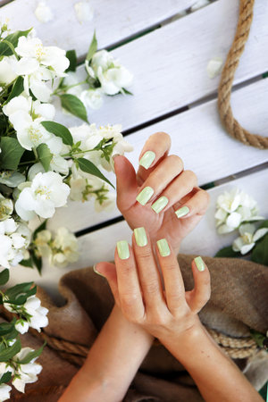 Women's hands with a green pastel manicure with jasmine on a wooden background with burlap.の写真素材