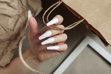 The extension of long white nails on a background with paper objects.の写真素材