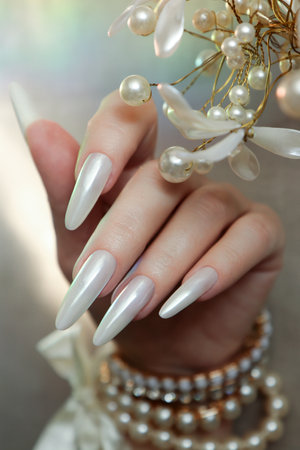 Female hand with long nails and white manicure with pearls and white flowersの写真素材