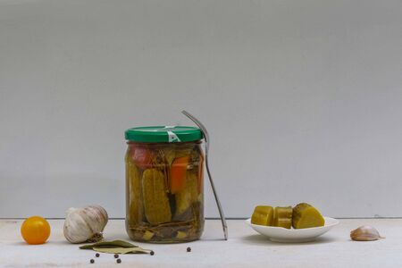 Pickled vegetables in a jar and on a cucumber on a plate, garlic and tomatoes on the table, horizontal orientation.の写真素材