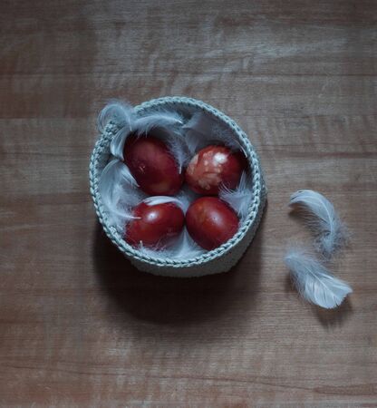 four red easter eggs on white feathers in a knitted basket