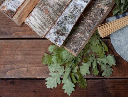 birch firewood and oak broom a bamboo massage broom for a sauna on a background of dark boards, top...