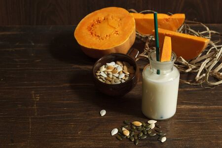 pumpkin vegetable raw milk, seeds in a brown bowl on a dark wooden table with chopped pumpkin in the background, view from above with spaceの写真素材