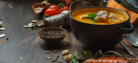 Pumpkin soup with croutons in a black mask and ingredients for cooking and on a dark wooden table, close -upの写真素材