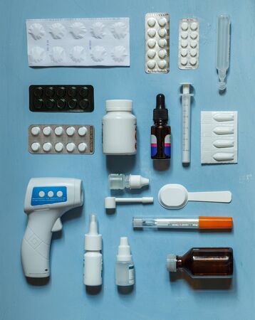 flatlay with tablets, medicines, drops, vials, measuring spoons and thermometers laid out on a blue backgroundの写真素材