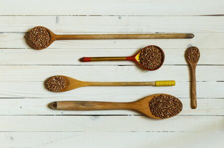 buckwheat grains in wooden spoons of different lengths on a light wooden background, top view