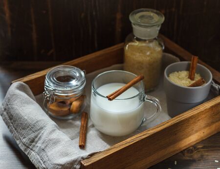 vegetarian rice milk in a glass Cup, cookies in a small jar and rice grains on a linen napkin in a wooden tray with crackers, dark wooden backgroundの写真素材
