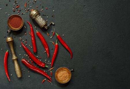 Red pepper pods, dried baby paprika and pepper peas with copper cooking utensils on a black table...