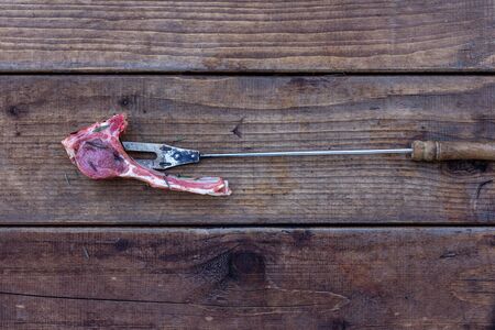 Raw lamb rib with rosemary on a barbecue fork, on rough wooden planks, top viewの写真素材