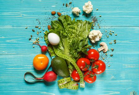 Tomatoes, green lettuce, radishes, eggs and avocado with measuring tape on blue boards