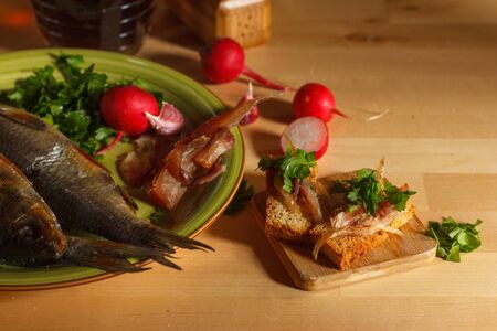croutons with smoked fish and herbs and roach on a plate with radishes and parsley on a light wooden...