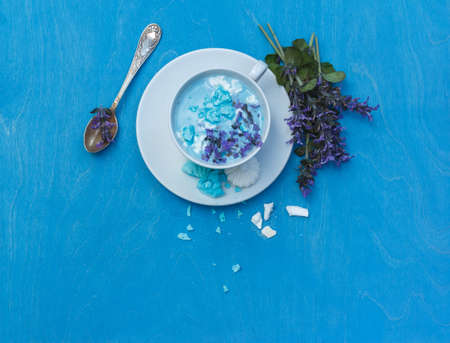 Layout with a Cup of blue moon milk with meringue and Melissa flowers.Top view with space, on a blue backgroundの写真素材