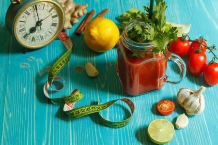 Tomato, lime and celery smoothies in a glass Cup, on a blue background with a centimeter and a clock
