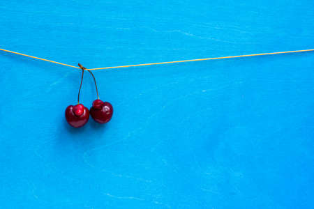 a pair of funny cherries of non-standard shape on a rope, on a bright blue background with space
