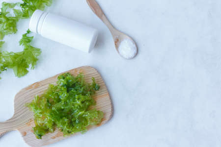 raw Ulva seaweed leaves on a wooden Board, seaweed powder and white bottle, light background with spaceの写真素材