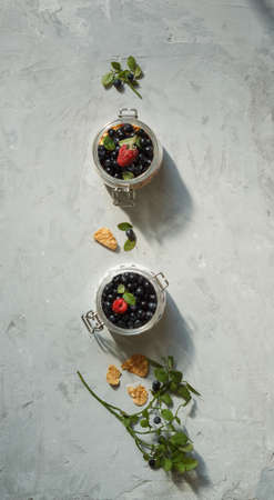 Desserts made from fresh berries in small glass jars. Layout on a grey background, verticallyの写真素材