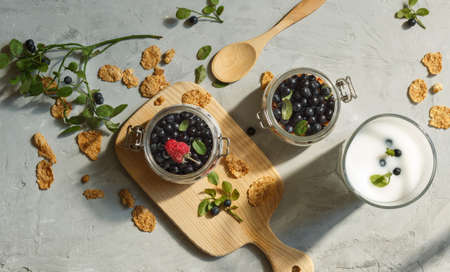 Top view of jars of fresh blueberries and raspberries and a glass of milk with berries on a gray...