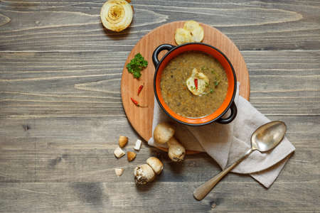 A portion of mushroom soup in a bowl, served on a round wooden Board with chips and hot pepper. Top view on a wooden background, with spaceの写真素材