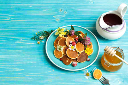 small pancakes with berries on a blue plate. With a jug of syrup and a jar of honey. On a blue...