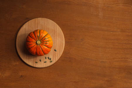 Orange small pumpkin on a round wooden stand. Wooden background with space for text. Horizontally, the topの写真素材