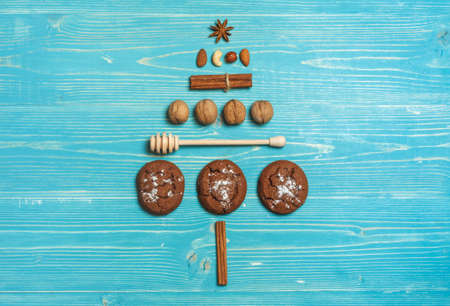 Cookies, nuts and spices laid out in the shape of a Christmas tree on a blue wooden background. Top...