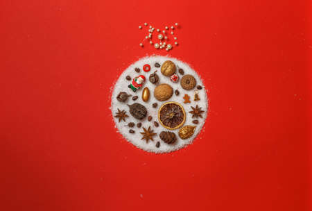 Decorations for the Christmas tree, gilded nuts, cones and toys laid out in the form of a Christmas ball with artificial snow. On a red background, top view with spaceの写真素材