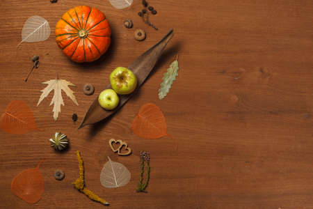 Autumn flatlay on a wooden background with orange pumpkin, apples and dry leaves. Horizontally with space for text.の写真素材